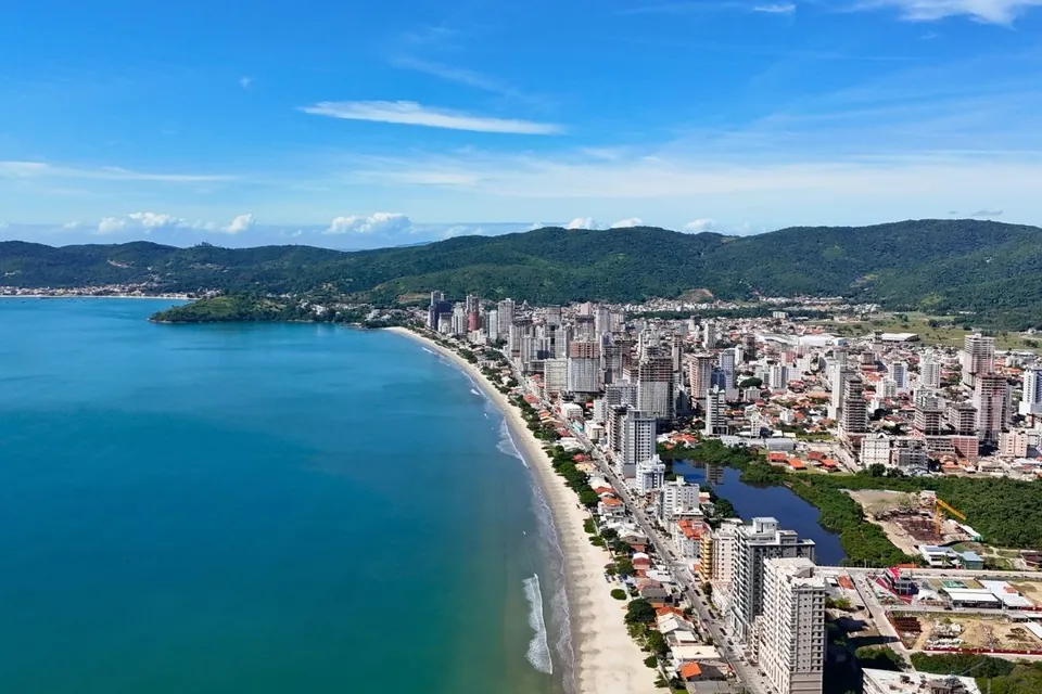 Vista aérea da orla, com o mar, a faixa de areia e os morros ao fundo